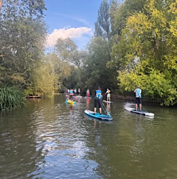 Stand up paddleboarders Paddleboarding down an english river bordered by trees